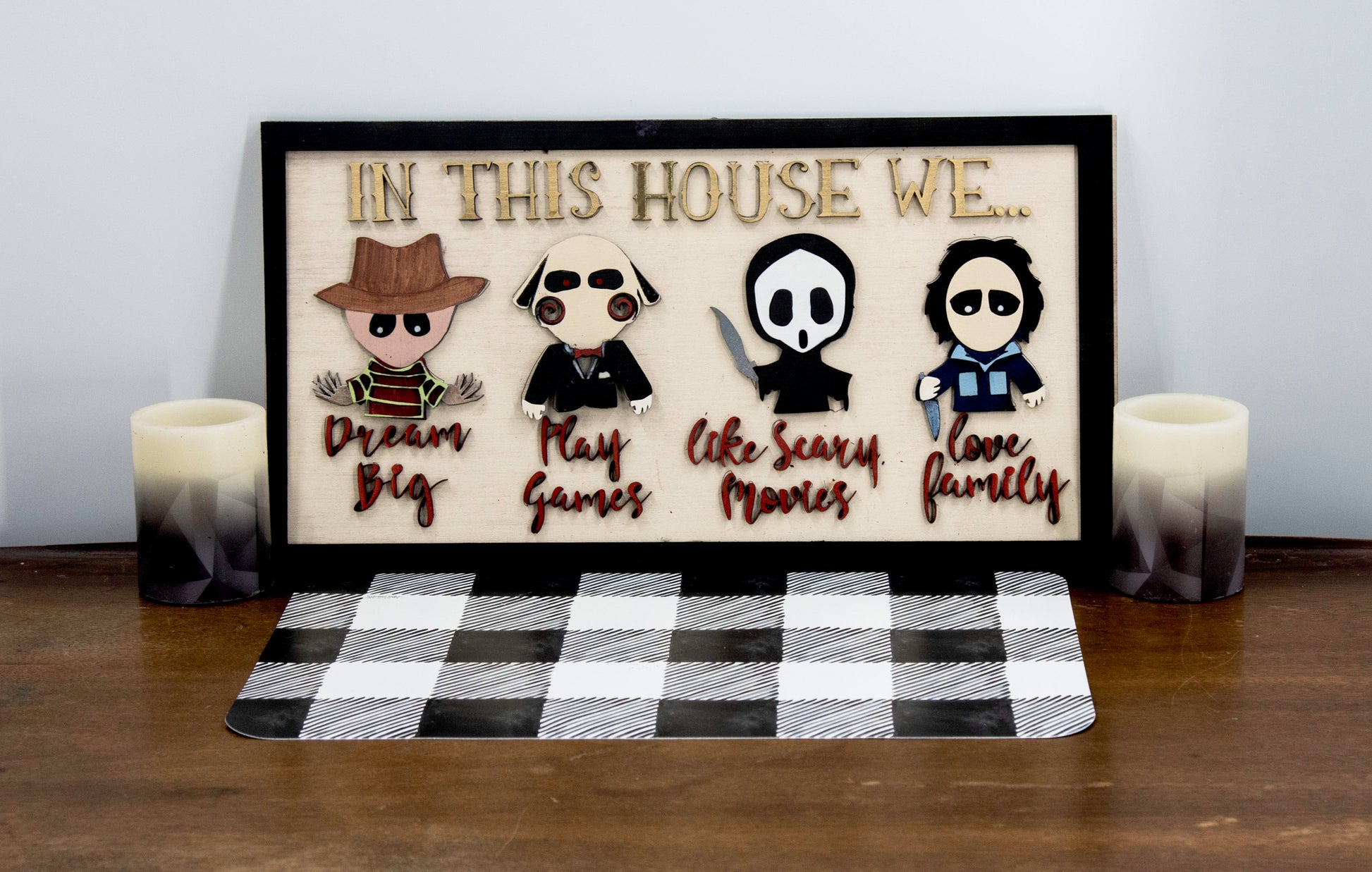 Wooden Halloween sign featuring layered cutout horror movie characters with engraved phrase “In This House,” handcrafted and freestanding, designed for spooky home decor fans.
