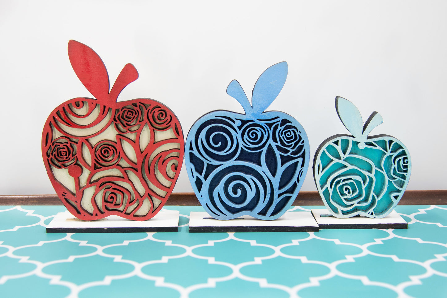 A handcrafted set of three standing wooden apple shelf sitters in assorted fall colors and patterns. These tiered tray-ready decorations include a rustic base and patterned top layer. Available individually or as a complete set, they bring warmth and charm to autumn home decor, classroom displays, or teacher gifts. Sizes range from 3.75" to 5.5".
