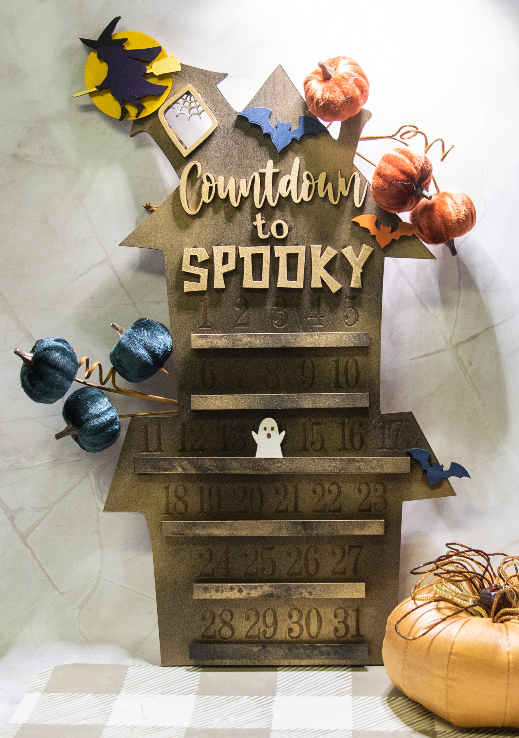 Wooden haunted house-themed Halloween countdown sign with engraved numbers from 1 to 31, painted in classic spooky colors like black, orange, and purple. Features a large haunted mansion design with bats, ghosts, and interchangeable marker icons to track the days until Halloween. Freestanding and available in two sizes, this layered wood sign is perfect for holiday decorating on a mantel, entryway, or shelf display.
