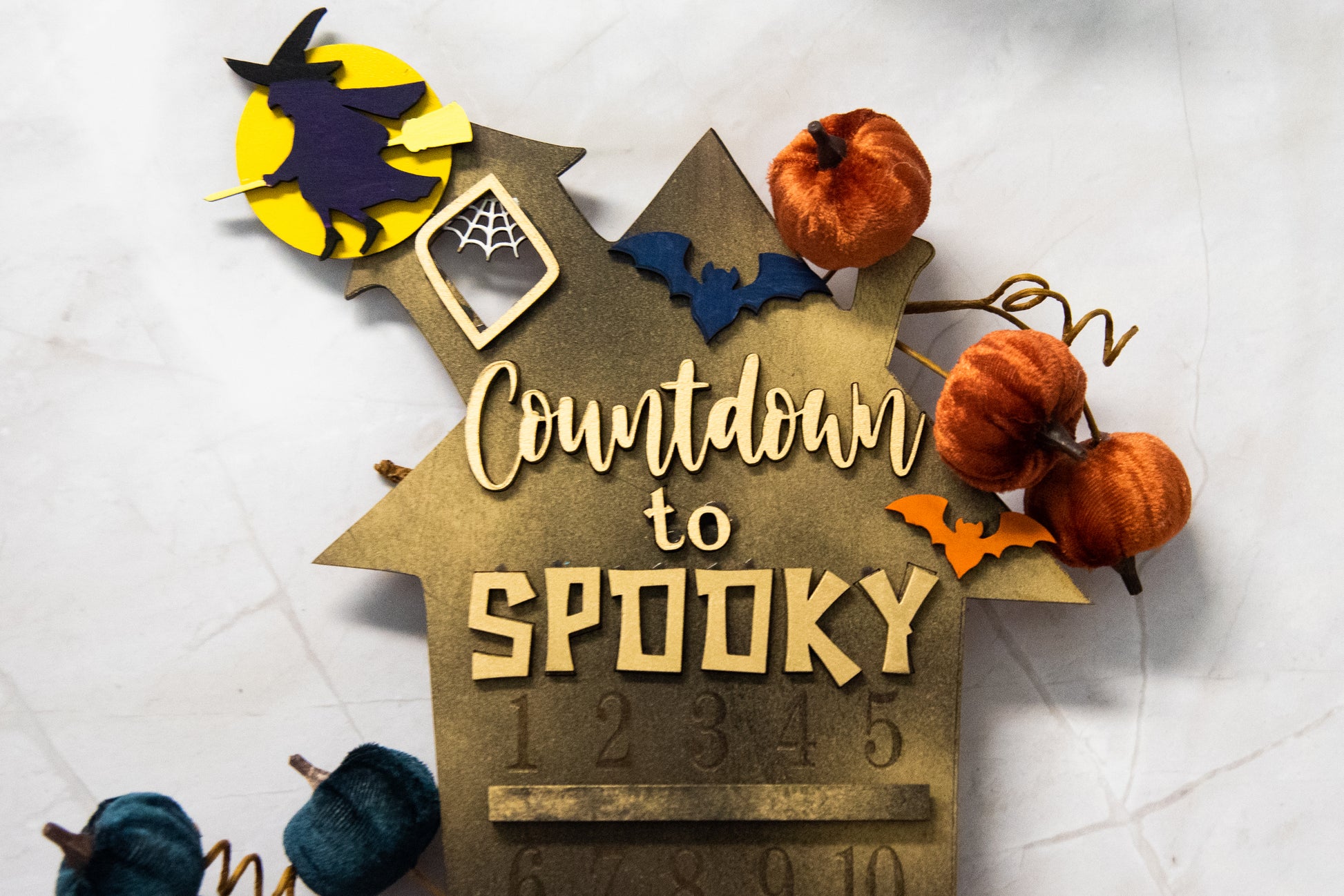 Wooden haunted house-themed Halloween countdown sign with engraved numbers from 1 to 31, painted in classic spooky colors like black, orange, and purple. Features a large haunted mansion design with bats, ghosts, and interchangeable marker icons to track the days until Halloween. Freestanding and available in two sizes, this layered wood sign is perfect for holiday decorating on a mantel, entryway, or shelf display.
