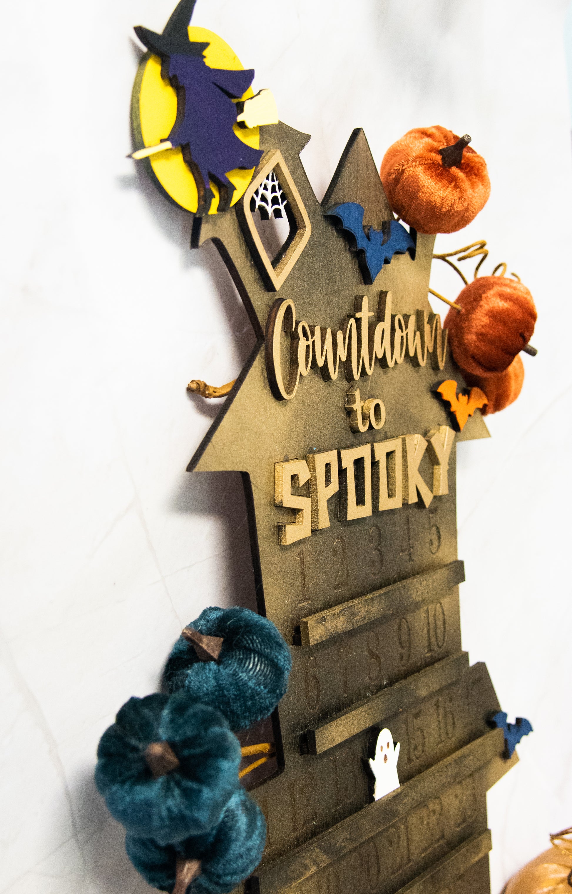 Wooden haunted house-themed Halloween countdown sign with engraved numbers from 1 to 31, painted in classic spooky colors like black, orange, and purple. Features a large haunted mansion design with bats, ghosts, and interchangeable marker icons to track the days until Halloween. Freestanding and available in two sizes, this layered wood sign is perfect for holiday decorating on a mantel, entryway, or shelf display.
