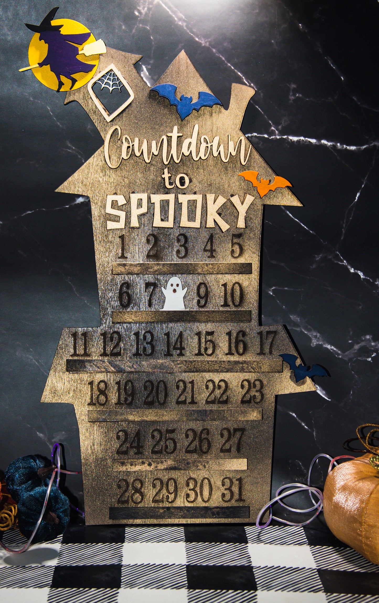 Wooden haunted house-themed Halloween countdown sign with engraved numbers from 1 to 31, painted in classic spooky colors like black, orange, and purple. Features a large haunted mansion design with bats, ghosts, and interchangeable marker icons to track the days until Halloween. Freestanding and available in two sizes, this layered wood sign is perfect for holiday decorating on a mantel, entryway, or shelf display.
