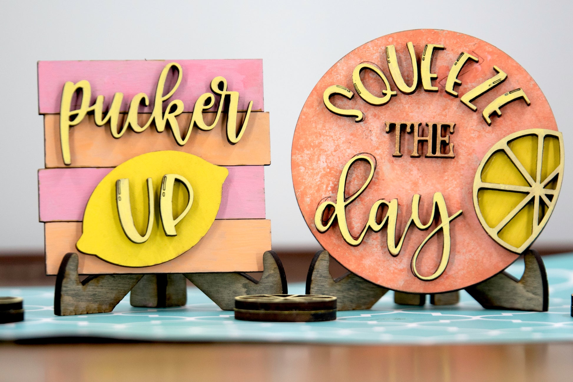 Hand-painted lemonade-themed tiered tray set featuring five wooden decor pieces in pastel pink, yellow, and orange. Includes lemon slice accents, banner flags, and stands for each item. Optional matching wooden tray base available