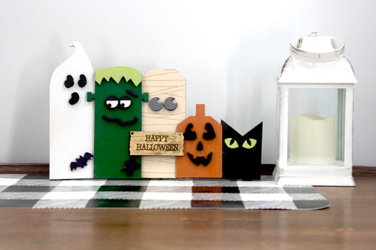 Layered wooden Halloween character shelf sitter set featuring Frankenstein, ghost, black cat, pumpkin, and tombstone. Includes interchangeable face designs, personalized sign text, and multiple size options for Halloween home decor.