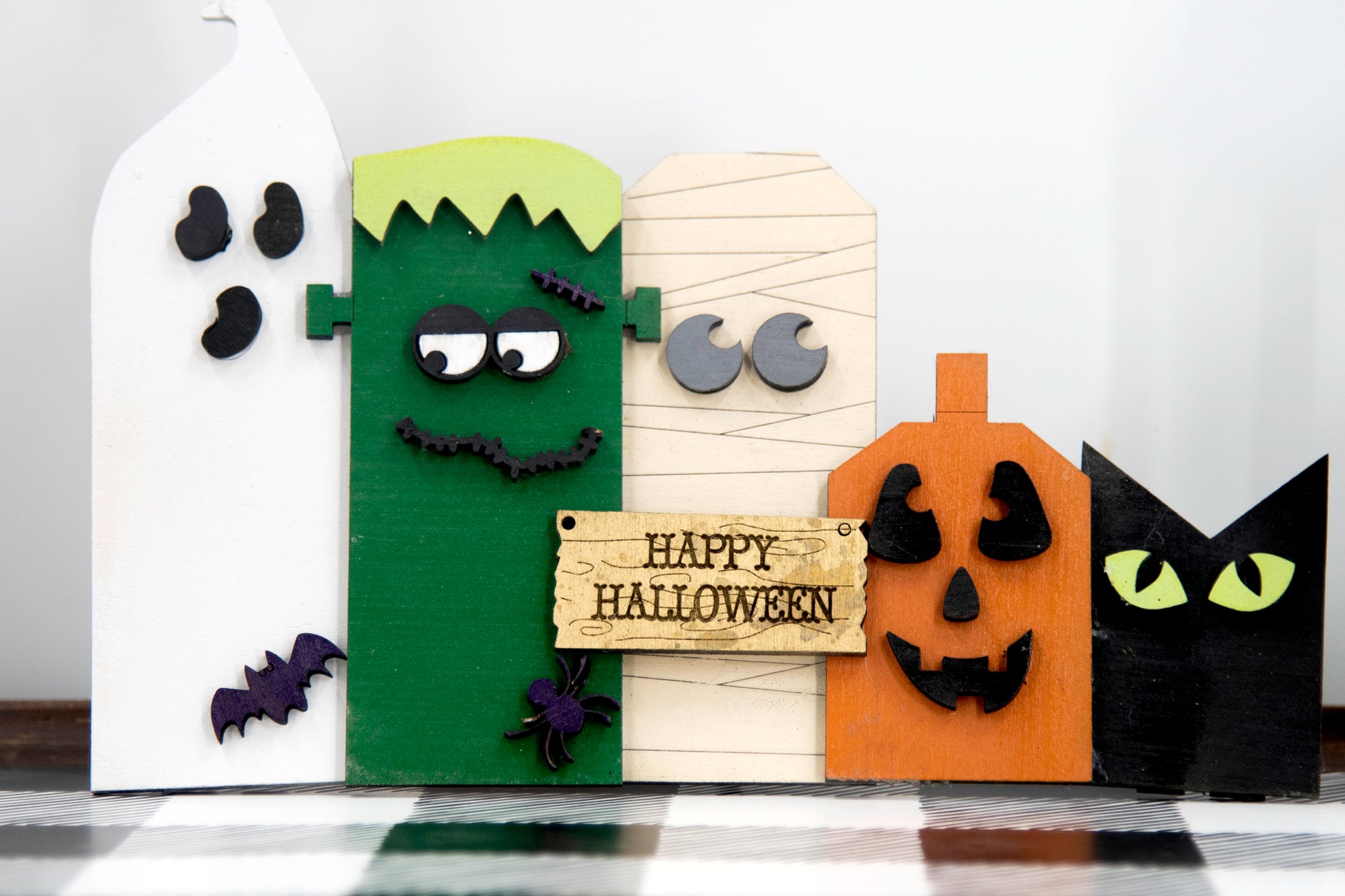 Layered wooden Halloween character shelf sitter set featuring Frankenstein, ghost, black cat, pumpkin, and tombstone. Includes interchangeable face designs, personalized sign text, and multiple size options for Halloween home decor.