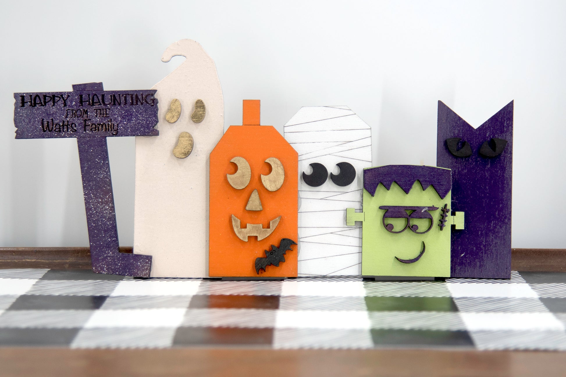 Layered wooden Halloween character shelf sitter set featuring Frankenstein, ghost, black cat, pumpkin, and tombstone. Includes interchangeable face designs, personalized sign text, and multiple size options for Halloween home decor.