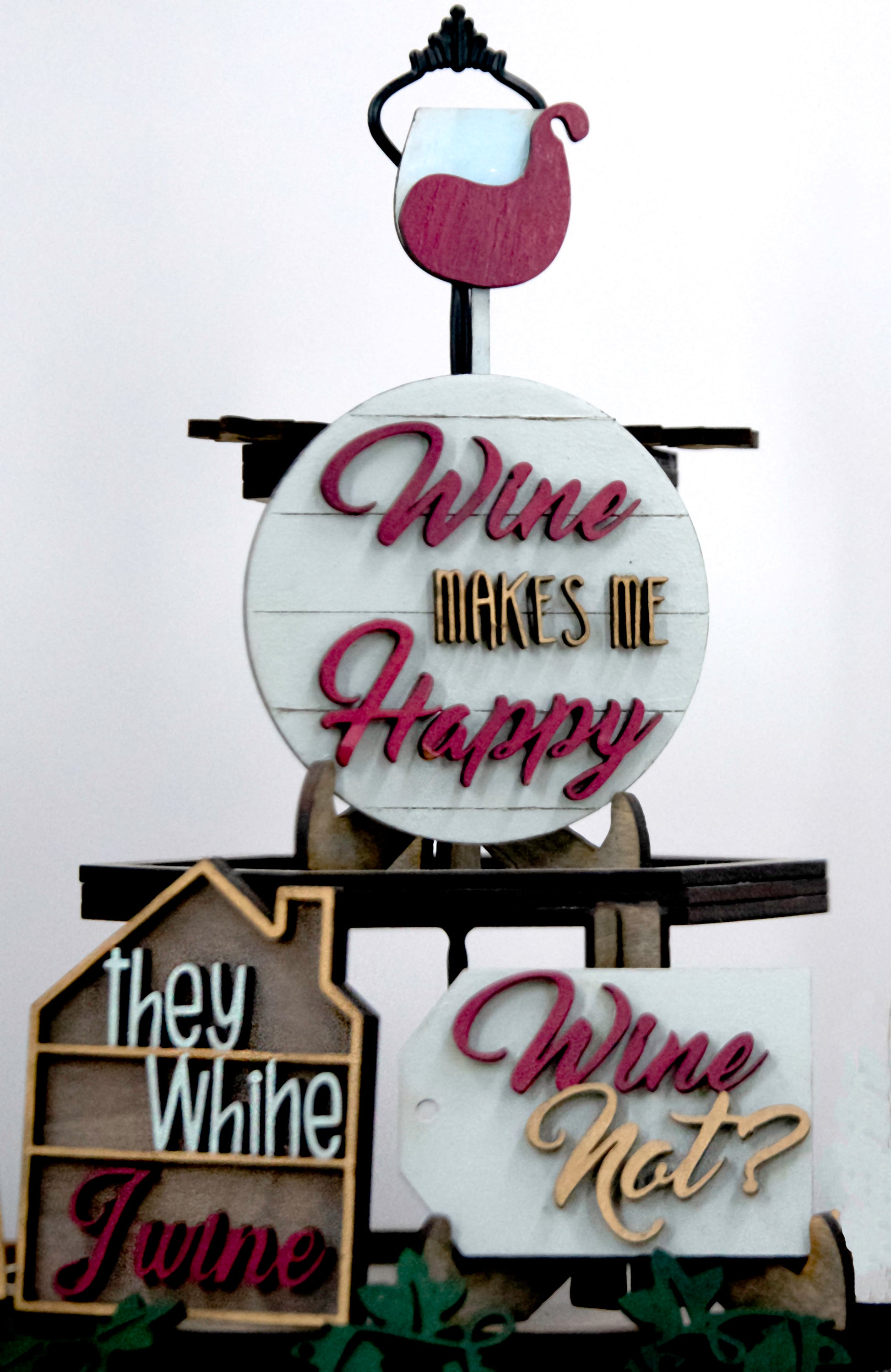 A 6-piece wine-themed wooden tiered tray set featuring humorous mom quotes like "They whine, I wine" and "Mommy juice," painted in maroon, grey, gold, and light grey with included stands and optional tiered tray
