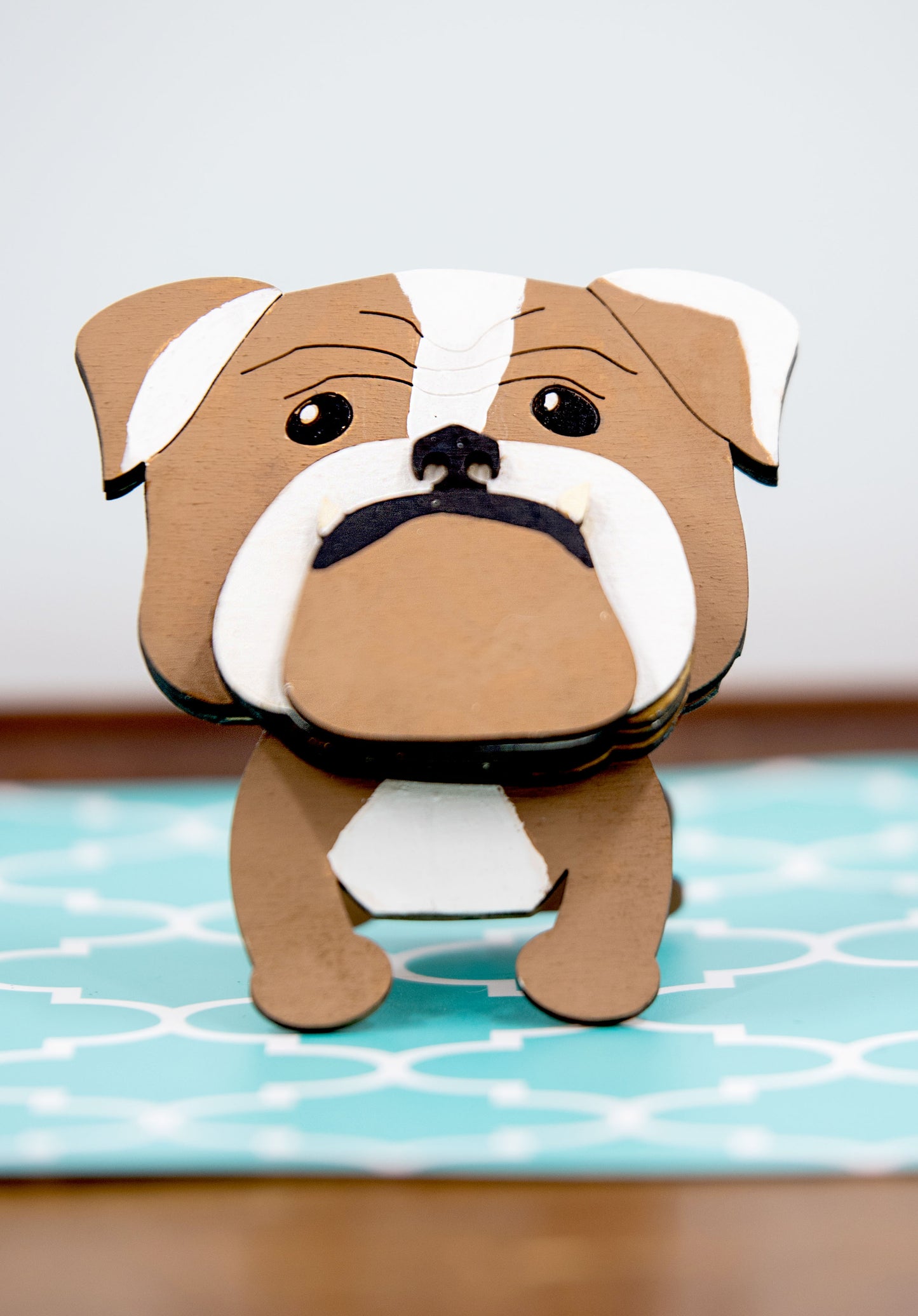 A hand-painted wooden glasses stand shaped like the face of an English Bulldog, featuring the breed’s signature wrinkled face and droopy cheeks. Designed with a flat base for stability, the stand holds eyeglasses securely on the Bulldog’s nose, making it a functional and charming decor piece for desks, nightstands, or shelves.
