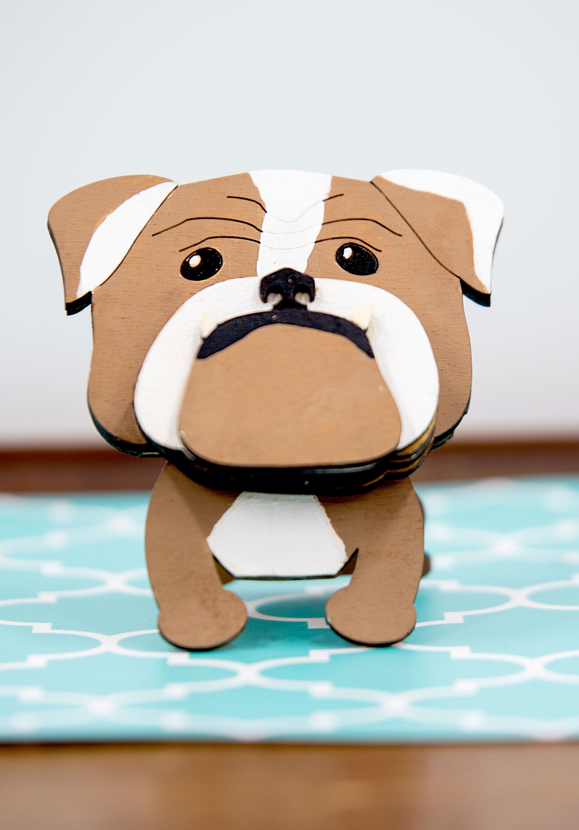 A hand-painted wooden glasses stand shaped like the face of an English Bulldog, featuring the breed’s signature wrinkled face and droopy cheeks. Designed with a flat base for stability, the stand holds eyeglasses securely on the Bulldog’s nose, making it a functional and charming decor piece for desks, nightstands, or shelves.