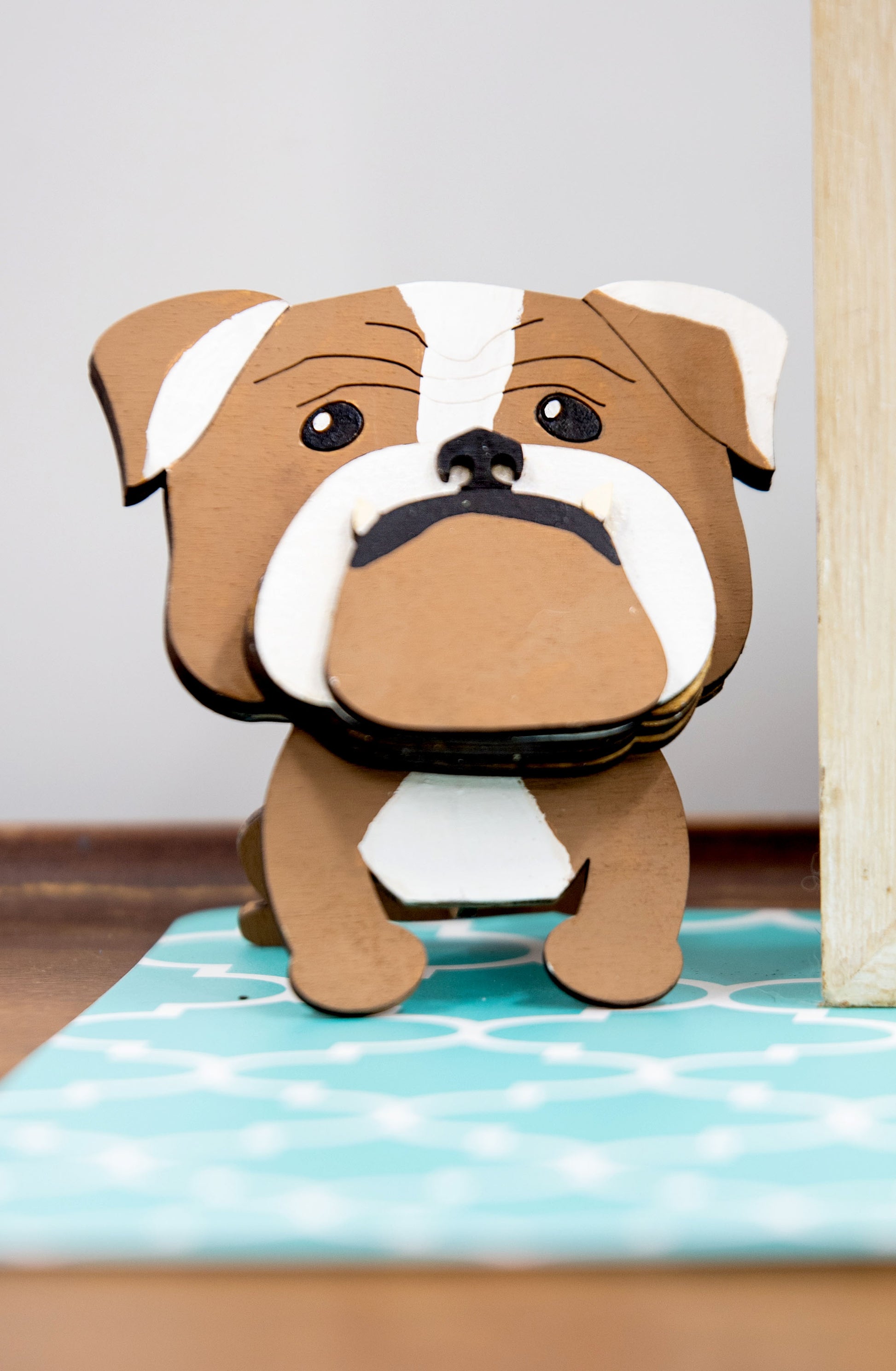 A hand-painted wooden glasses stand shaped like the face of an English Bulldog, featuring the breed’s signature wrinkled face and droopy cheeks. Designed with a flat base for stability, the stand holds eyeglasses securely on the Bulldog’s nose, making it a functional and charming decor piece for desks, nightstands, or shelves.