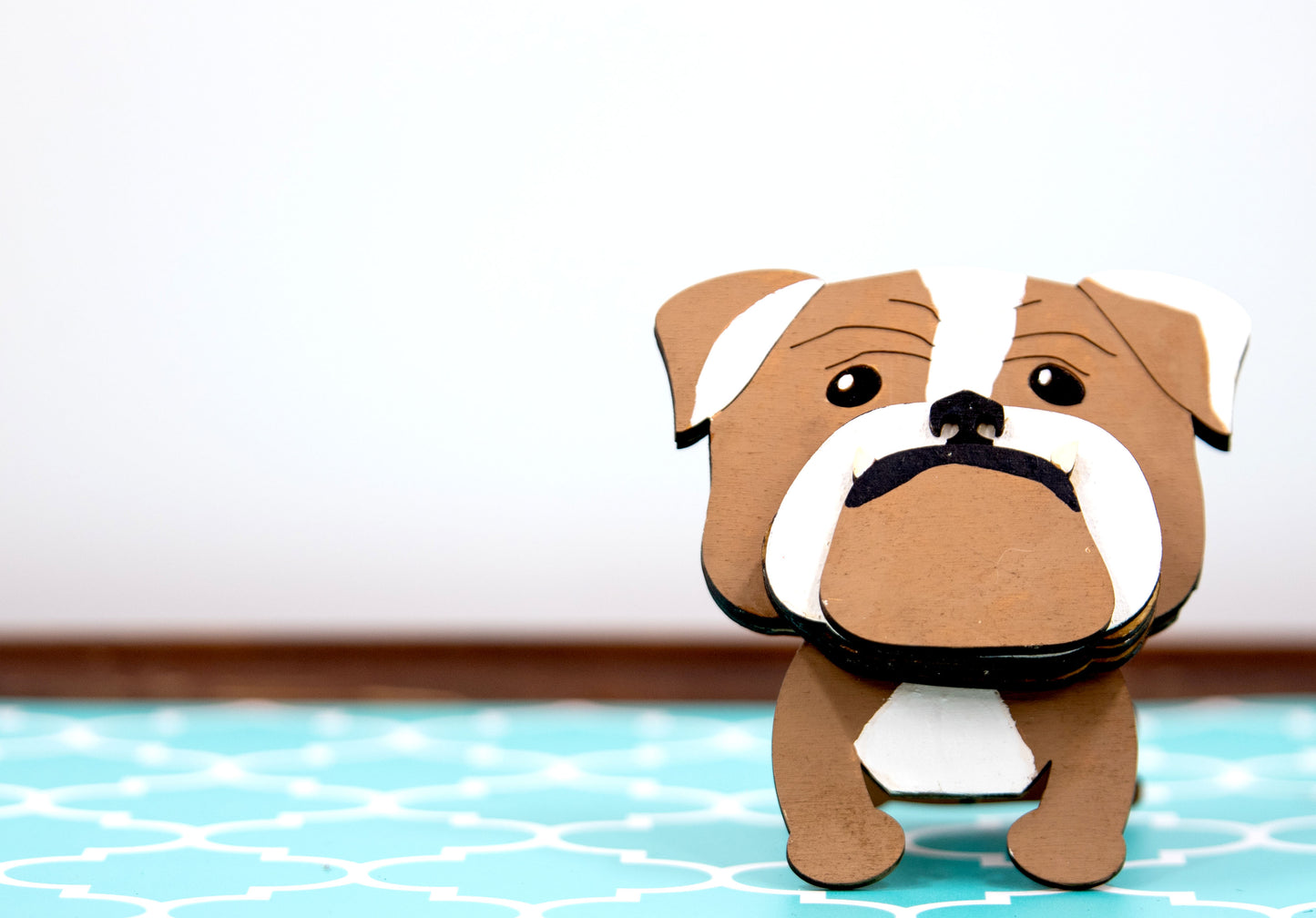 A hand-painted wooden glasses stand shaped like the face of an English Bulldog, featuring the breed’s signature wrinkled face and droopy cheeks. Designed with a flat base for stability, the stand holds eyeglasses securely on the Bulldog’s nose, making it a functional and charming decor piece for desks, nightstands, or shelves.