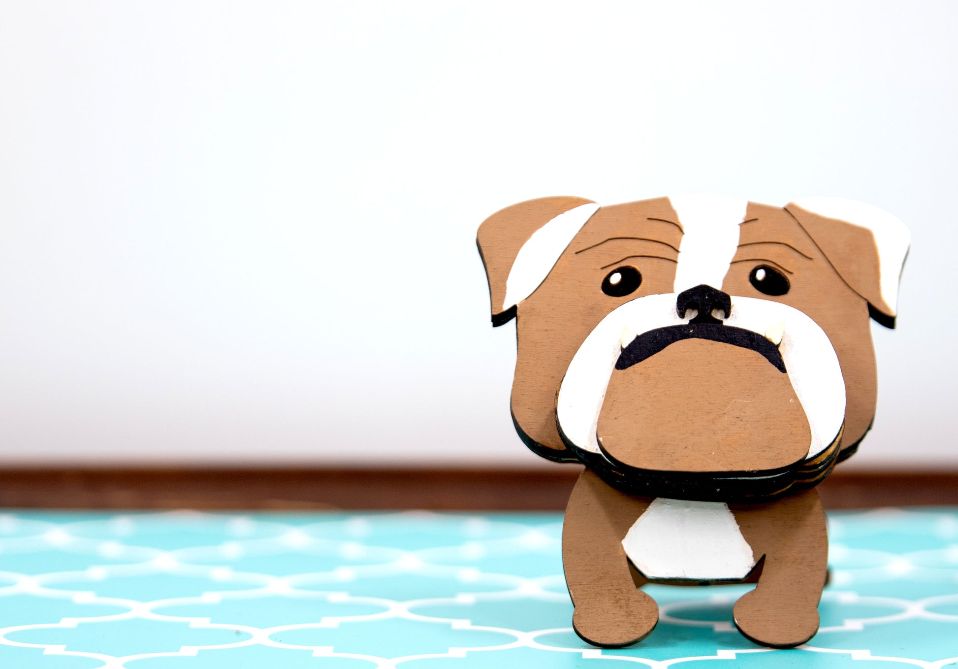A hand-painted wooden glasses stand shaped like the face of an English Bulldog, featuring the breed’s signature wrinkled face and droopy cheeks. Designed with a flat base for stability, the stand holds eyeglasses securely on the Bulldog’s nose, making it a functional and charming decor piece for desks, nightstands, or shelves.
