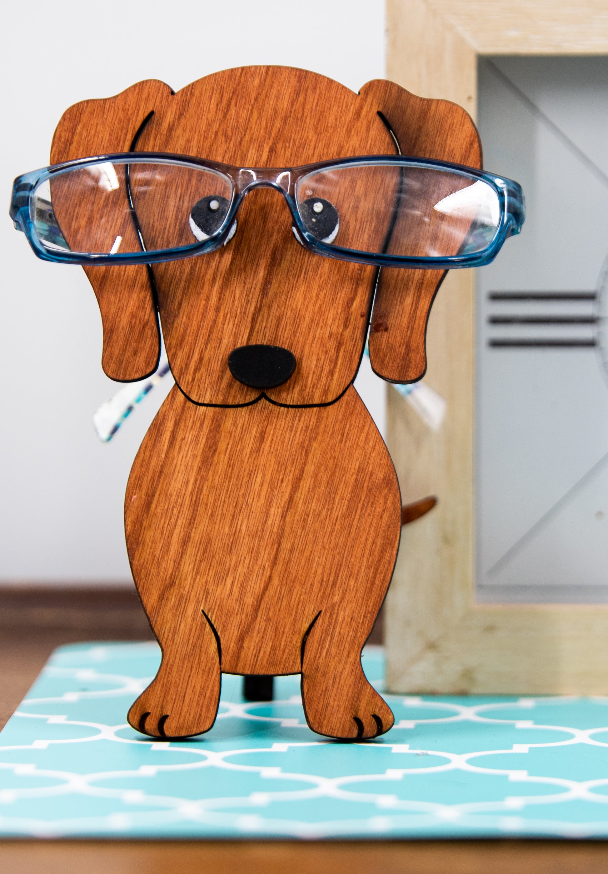 Large stained dachshund glasses holder made from solid wood, shown in red/brown finish, designed to keep eyeglasses secure while adding charm to your decor. Handmade eyeglass stand shaped like a dachshund with adorable detailing, perfect for bedside tables, desks, or as a thoughtful gift for dog lovers. Available in red/brown, black, or custom stain colors to match your style.