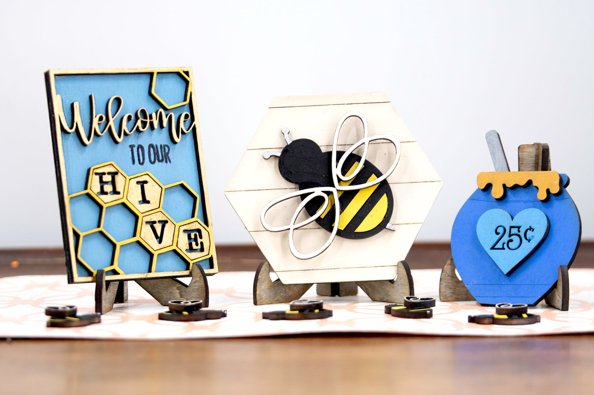 DIY bee tiered tray kit with 6 unfinished wood pieces including honey jar, local honey sign, welcome to our hive sign, honey bomb, bee hexagon plaque, and 5 small bee accents. Ideal for painting, staining, and customizing. Comes with stands for easy display. Perfect for summer crafts, farmhouse style decor, or paint-your-own projects. Great for hobby crafters, DIY parties, and seasonal decorating fun with a bee and honey theme.
