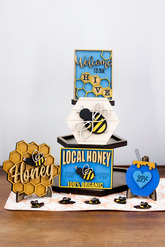 DIY bee tiered tray kit with 6 unfinished wood pieces including honey jar, local honey sign, welcome to our hive sign, honey bomb, bee hexagon plaque, and 5 small bee accents. Ideal for painting, staining, and customizing. Comes with stands for easy display. Perfect for summer crafts, farmhouse style decor, or paint-your-own projects. Great for hobby crafters, DIY parties, and seasonal decorating fun with a bee and honey theme.
