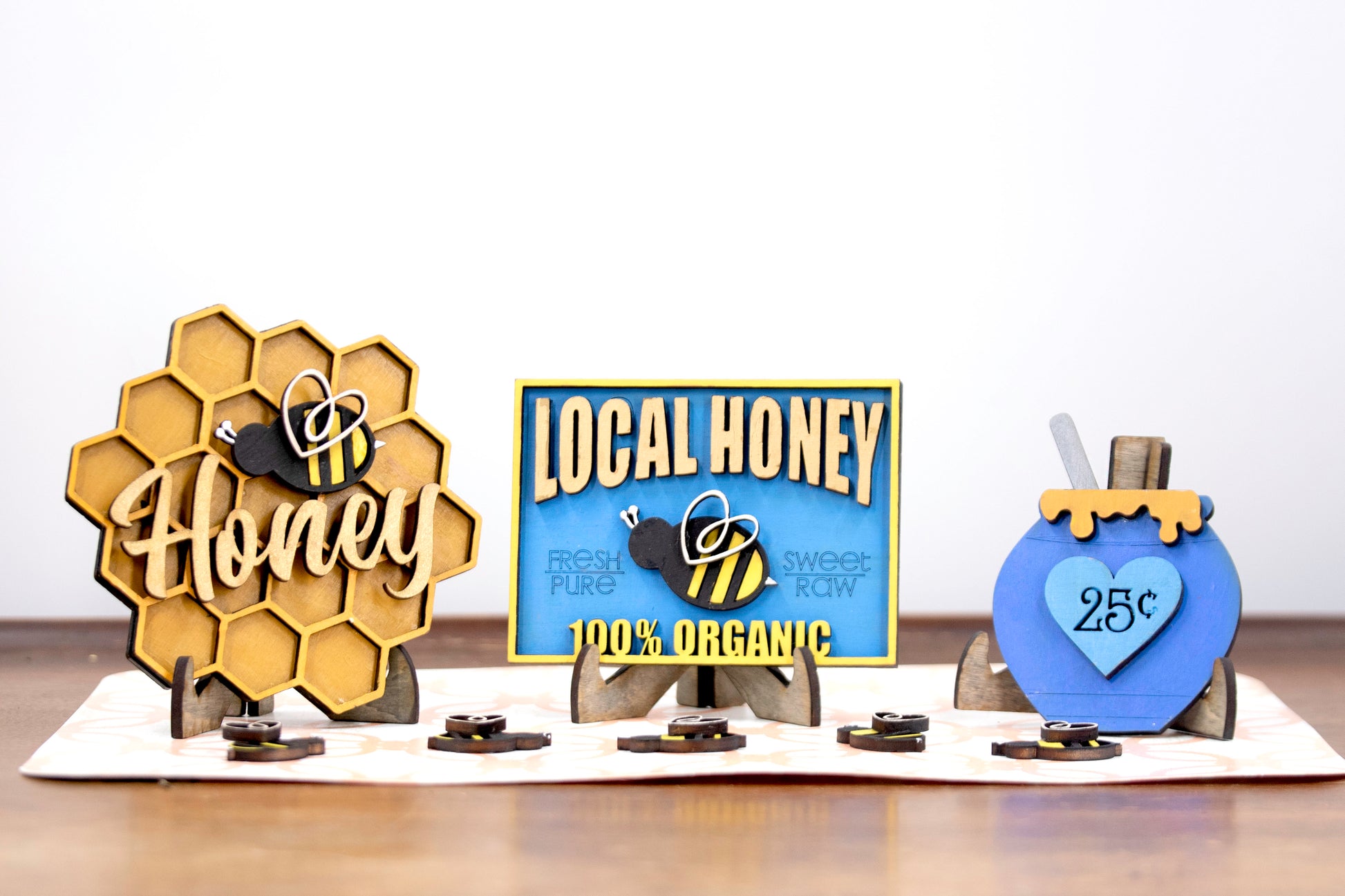 DIY bee tiered tray kit with 6 unfinished wood pieces including honey jar, local honey sign, welcome to our hive sign, honey bomb, bee hexagon plaque, and 5 small bee accents. Ideal for painting, staining, and customizing. Comes with stands for easy display. Perfect for summer crafts, farmhouse style decor, or paint-your-own projects. Great for hobby crafters, DIY parties, and seasonal decorating fun with a bee and honey theme.
