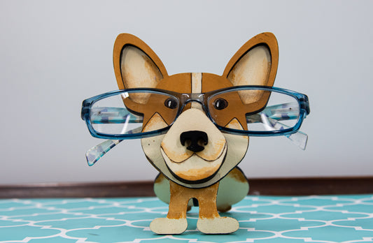 Adorable hand-painted wooden Corgi dog glasses holder stand, crafted as a whimsical eyeglass organizer and dog lover gift. Features a realistic Pembroke or Cardigan Corgi design with a notch to hold eyeglasses or sunglasses securely, perfect for quirky desk decor, pet-themed home accessories, or as a gift for Corgi enthusiasts.