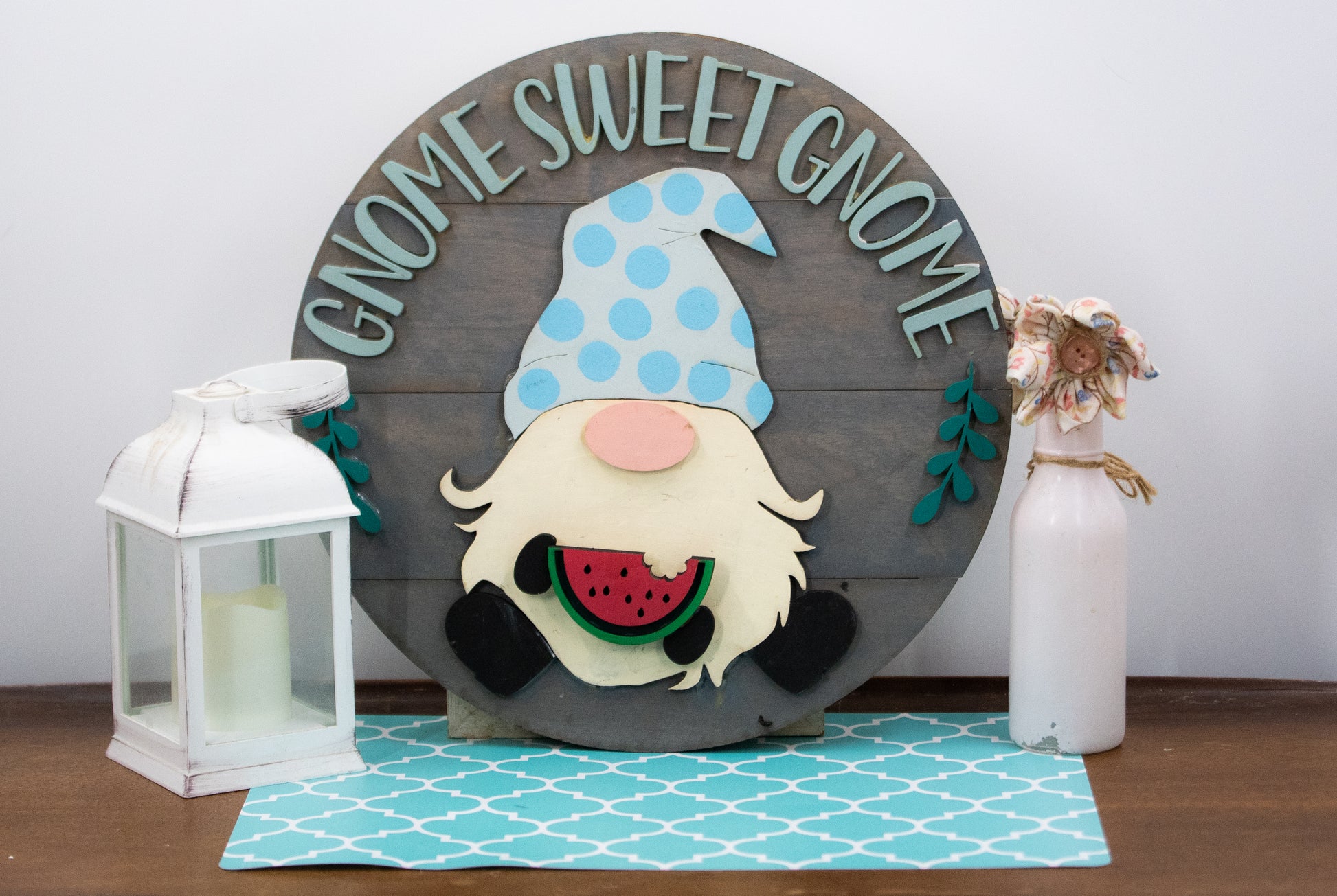 Interchangeable gnome sweet gnome round door sign with grey slatted wood base, engraved text, whimsical gnome holding one of 12 colorful seasonal pieces attached with velcro, perfect farmhouse rustic home decor for entryway or front door, customizable colors available.
