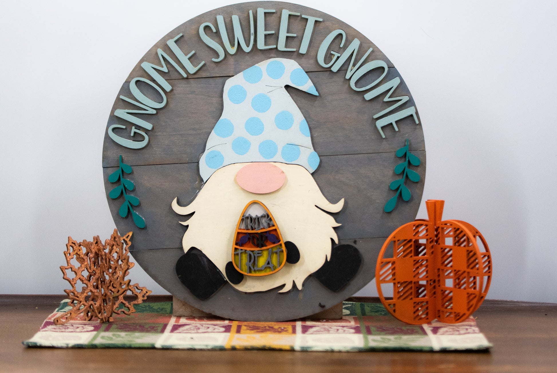 DIY kit for interchangeable gnome sweet gnome round sign with unfinished grey slatted wood base, engraved text, whimsical gnome figure, and 12 blank seasonal pieces with velcro for painting and assembly, farmhouse rustic decor craft project for entryway or door.
