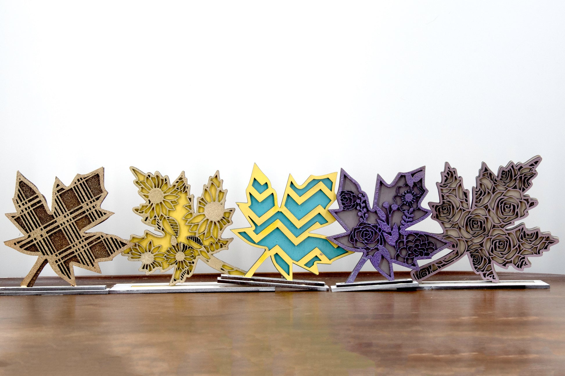 Set of freestanding wooden leaf shelf sitters with two-layer designs, featuring colorful stained bases and patterned top cutouts in fall-themed shapes. These decorative leaves range in size from 3" to 6" tall and are ideal for mantels, tiered trays, and autumn home displays. Handcrafted, rustic, and available in custom colors. Perfect for fall decorating, Thanksgiving accents, and cozy seasonal vibes.
