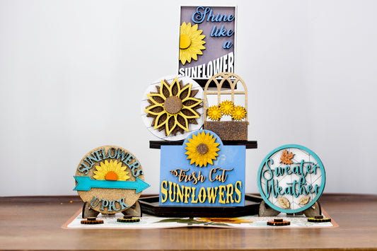 Sunflower-themed tiered tray set with six detailed pieces including signs like “Shine Like a Sunflower,” “Fresh Cut Sunflowers,” and “U Pick.” Includes a 6" faux slatted round with a sunflower graphic, window box, sweater weather sign, and five mini sunflower accents. Rustic farmhouse style in bright yellows and soft neutrals. Optional hexagon tray available. Perfect for fall or summer seasonal decor and kitchen styling.
