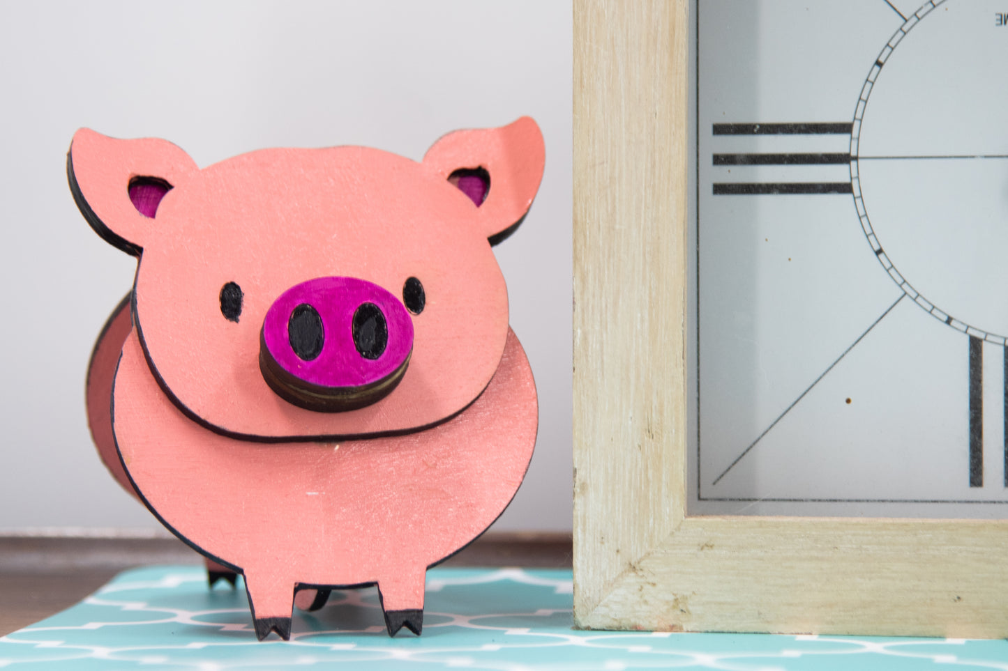 Handcrafted wooden pig-shaped eyeglass stand with pink finish and black details, holding glasses on its snout, ideal for desks or gift giving.