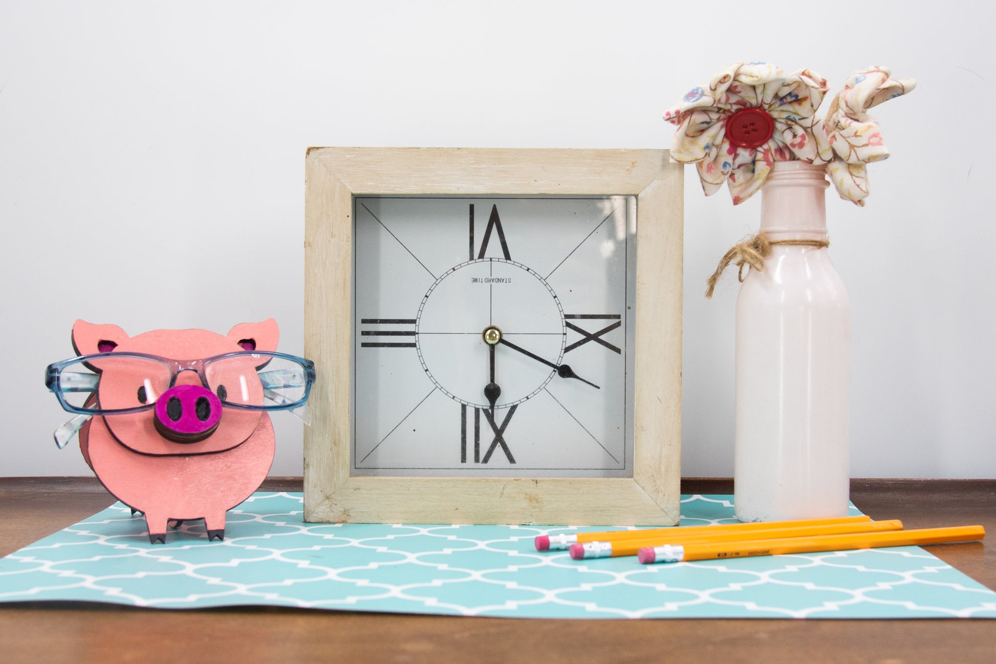 Handcrafted wooden pig-shaped eyeglass stand with pink finish and black details, holding glasses on its snout, ideal for desks or gift giving.