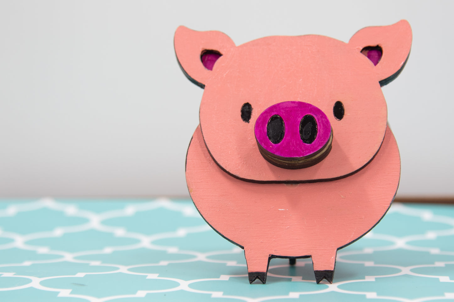 Handcrafted wooden pig-shaped eyeglass stand with pink finish and black details, holding glasses on its snout, ideal for desks or gift giving.