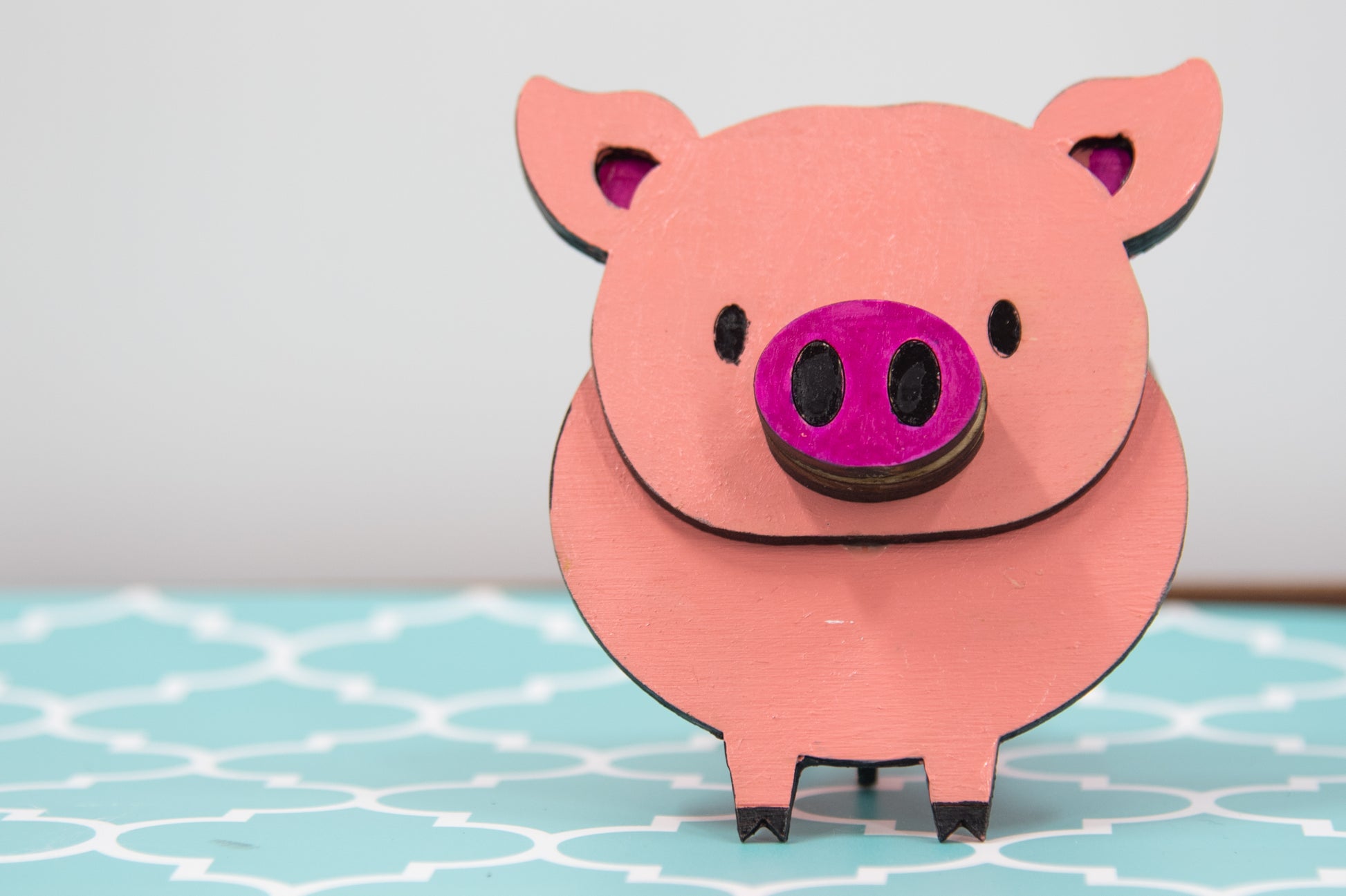 Handcrafted wooden pig-shaped eyeglass stand with pink finish and black details, holding glasses on its snout, ideal for desks or gift giving.