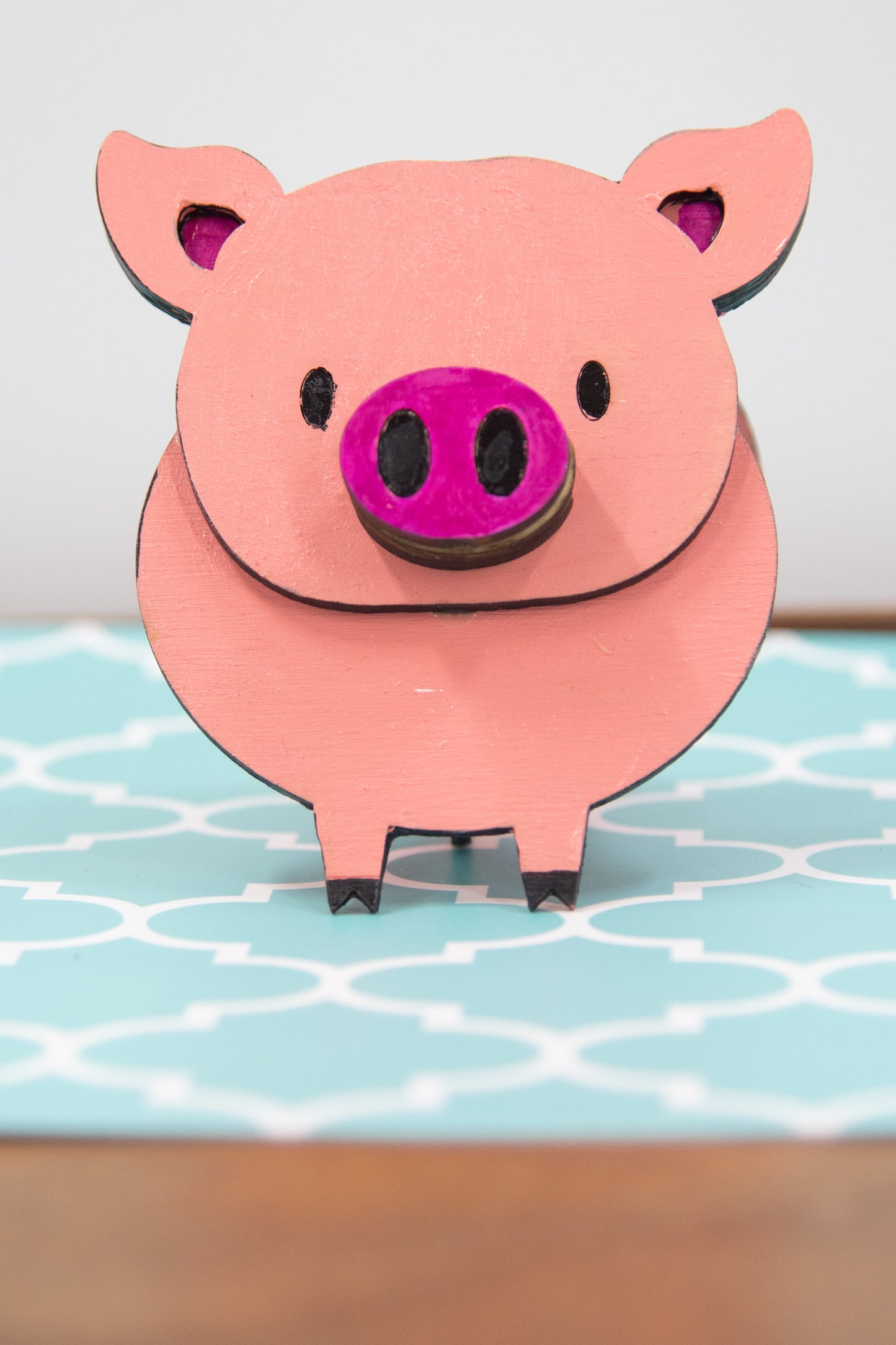 Handcrafted wooden pig-shaped eyeglass stand with pink finish and black details, holding glasses on its snout, ideal for desks or gift giving.