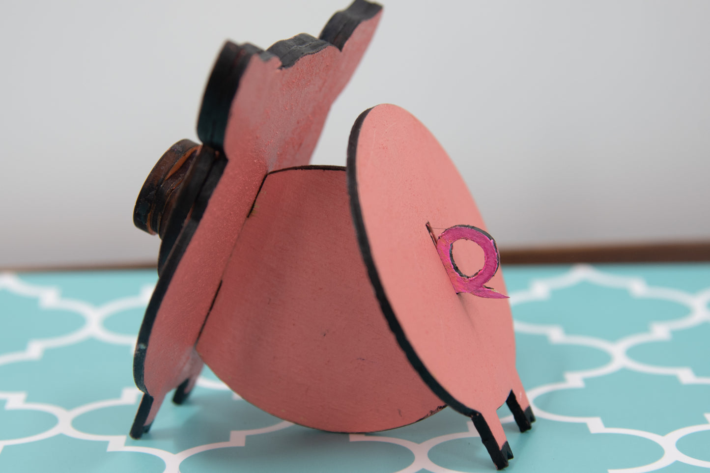 Handcrafted wooden pig-shaped eyeglass stand with pink finish and black details, holding glasses on its snout, ideal for desks or gift giving.