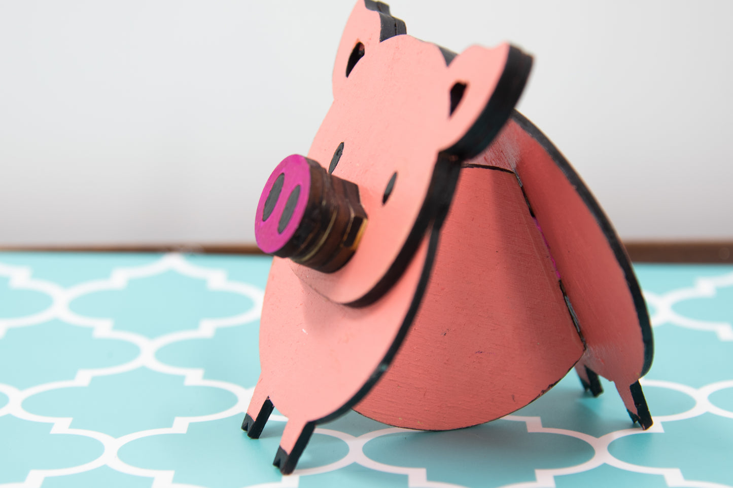 Handcrafted wooden pig-shaped eyeglass stand with pink finish and black details, holding glasses on its snout, ideal for desks or gift giving.