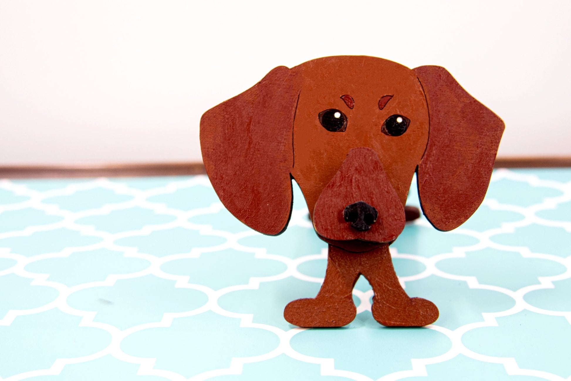 Close- up of a handmade dachshund eyeglass holder with brown paint and carved features, Made to hold reading glasses securely.
